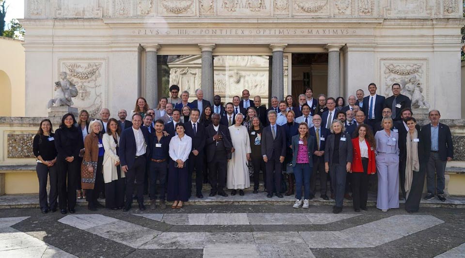 A large group of people stand and pose in front of a building at the Vatican.