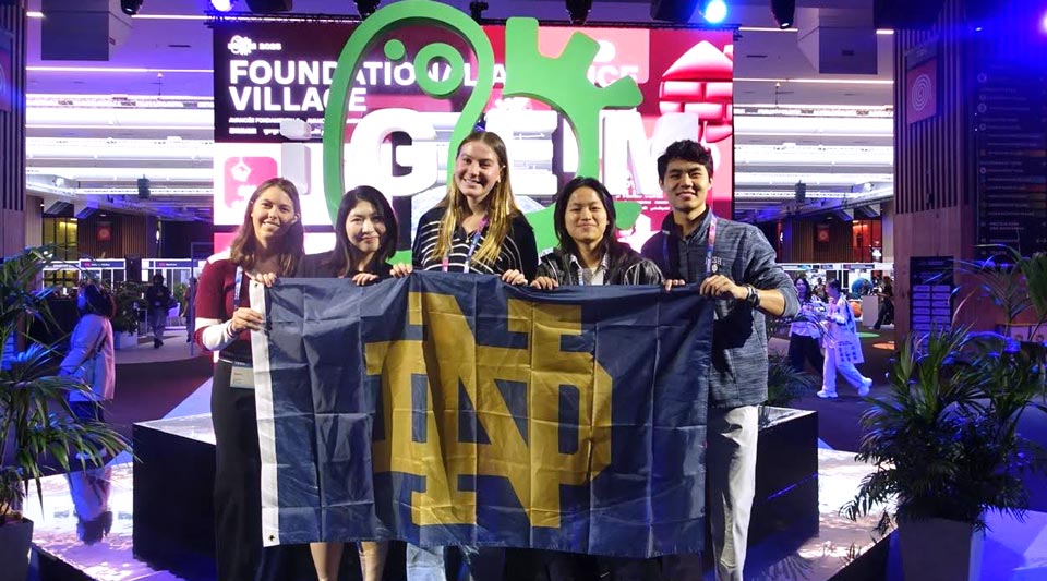 A group of students pose with a flag bearing the ND monogram.